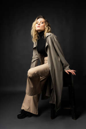 Beautiful girl wearing a casual trendy trousers, turtleneck and raincoat posing on a dark background. Fashionable, advertising, lifestyle and commercial designの写真素材