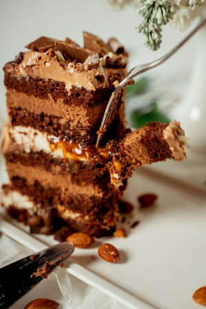 Chocolate cake decorated with various cookies and nuts on a glass plate and macaroons among white flowers of lilac and green leaves. Food photography. Advertising and commercial close up designの写真素材
