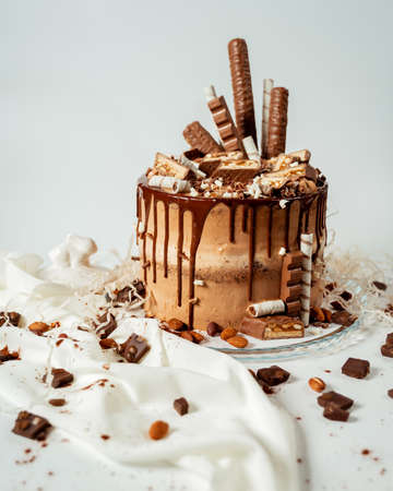 Chocolate cake decorated with various cookies and nuts on a glass plate standing on a white cloth. Food photography. Advertising and commercial close up designの写真素材