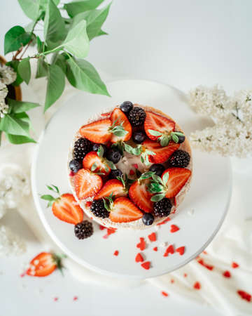 White berry cream cake decorated with strawberries and blackberries, among lilac flowers and green leaves. Food photography. Advertising and commercial close up designの写真素材