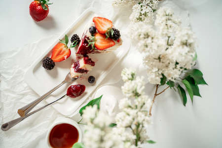 Sliced white berry cream cake decorated with strawberries and blackberries, among lilac flowers and green leaves. Food photography. Advertising and commercial close up designの写真素材