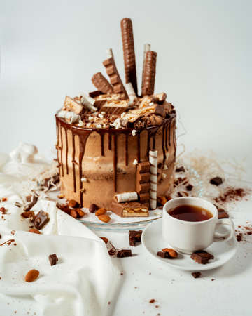 Chocolate cake decorated with various cookies and nuts on a glass plate standing on a white cloth. Food photography. Advertising and commercial close up designの写真素材
