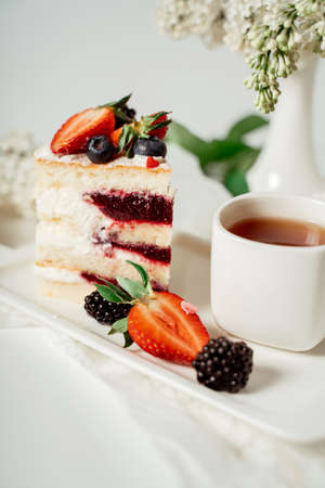 Sliced white berry cream cake decorated with strawberries and blackberries, among lilac flowers and green leaves. Food photography. Advertising and commercial close up designの写真素材
