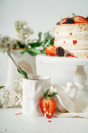 White berry cream cake decorated with strawberries and blackberries, among lilac flowers and green leaves. Food photography. Advertising and commercial close up designの写真素材