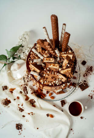 Chocolate cake decorated with various cookies and nuts on a glass plate standing on a white cloth. Food photography. Advertising and commercial close up designの写真素材