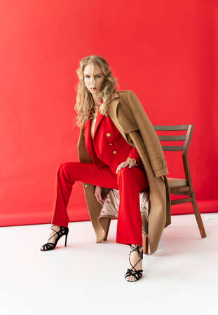 A beautiful blonde curly girl wearing a red pants and a blouse, unbuttoned on her braless big breasts, sensually poses, touching herself. Advertising, fashionable, commercial, design.の写真素材