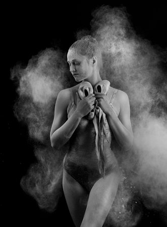 A beautiful slender ballet dancer girl wearing a bodysuit, sensually poses among the flying flour which covers her body, on a black background. Artistic, commercial, monochrome design.の写真素材