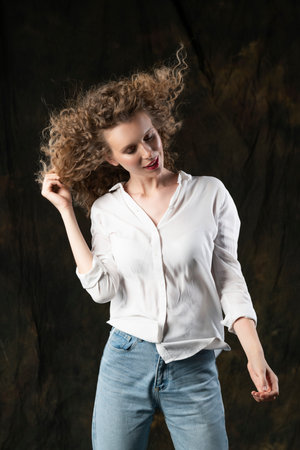 A beautiful girl, wearing jeans and a blouse, poses cheerfully in the wind, which blows her long curly hair and clothes. Advertising, commercial design.の写真素材