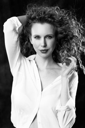 A beautiful girl, wearing jeans and a blouse, poses cheerfully in the wind, which blows her long curly hair and clothes. Close up. Advertising, commercial, monochrome design.の写真素材