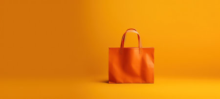 Stylish empty orange shopping bag against a vibrant yellow background, perfect for retail, consumerism, and fashion conceptsの素材