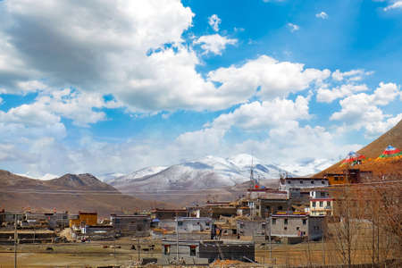 View of traditional Tibetan village against the Himalayan Mountains, against a blue sky covered by white clouds.の写真素材
