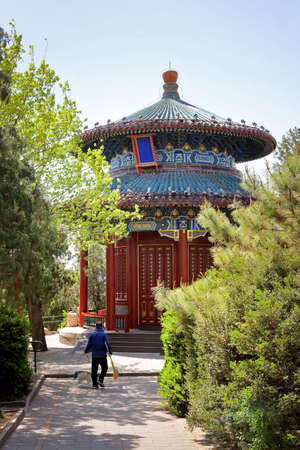 Man in front of a colorful red, blue, green and yellow building inside the Palace Museum, known also as the Forbidden City in Beijing, China, surrounded by green vegetation.の写真素材