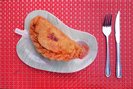 Chilean fried turnover called Empanada, consisting of pastry and tuna filling, served with a spicy sauce, traditionally eaten on Easter Island, on a red table cover made of plastic.の写真素材