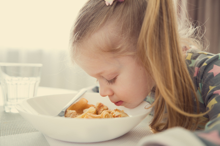 Close-up portrait of little girl with dinner. Child checking food in plate.の写真素材