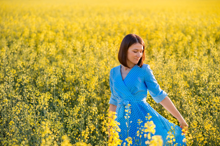 Summer nature. Young woman in blue dress walking on yellow field in the evening. Attractive girl outdoors enjoying fresh air. Allergy free theme.の写真素材