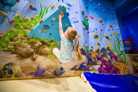 Little girl on climbing wall. Attractions for children. Kid sports theme. Overcomes difficulties.の写真素材
