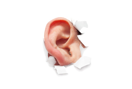 The human ear is sticking out of a hole in a paper isolatedの写真素材