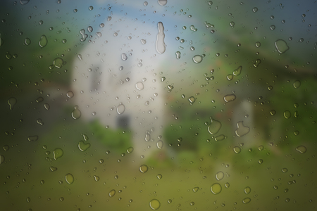 Rain drops on window glass and a cottage in the backgroundの写真素材