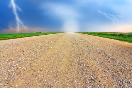 Country road through the field and storm aheadの写真素材