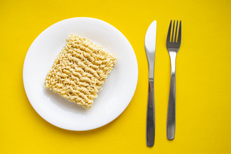 Noodles on a plate. Vermicelli in the shape of a square on a round plate. Fork and knife and noodles on a plate.の写真素材