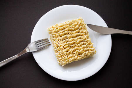 Noodles on a plate. Vermicelli in the shape of a square on a round plate. Fork and knife and noodles on a plate.の写真素材