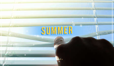 The sun shines through the half-open blinds on the window. Blinds ajar by hand. Summer inscription on the background of the sun. Summer is visible through the ajar blinds.の写真素材