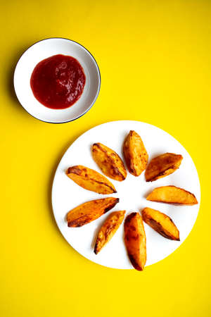 Fried fries and tomato sauce on a yellow background. Fast food. Rustic potatoes baked in the oven. Sliced and fried potatoes.の写真素材
