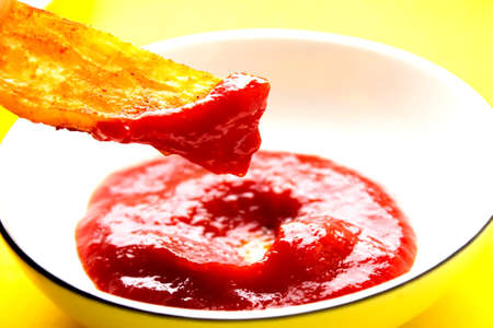 Fried fries and tomato sauce on a yellow background. Fast food. Rustic potatoes baked in the oven. Sliced and fried potatoes.の写真素材