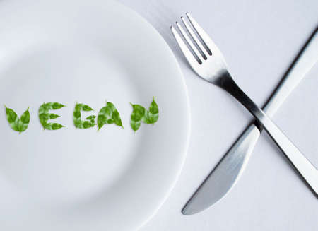 Vegan lettering made from leaves on a plate. The letters are composed of leaves folded into the word vegan. Healthy and wholesome food. Vegetarian food.の写真素材