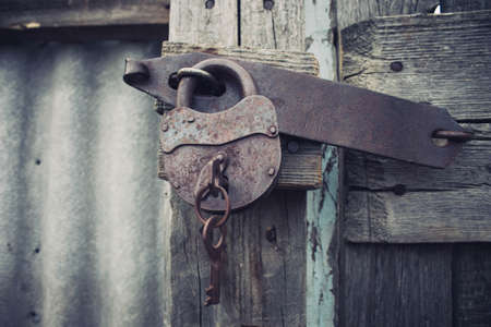 Iron rusty lock with a key. Closed door. Locked gates to the barn lock. Old locked shutters.