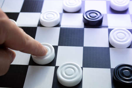 Board game of checkers. Black and white chips for the game. Chess field. Checkers move close-up. Checker in hand.の写真素材