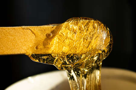 Sugar paste for hair removal. Shugaring paste close-up. Liquid sugar flows down a wooden spatula....