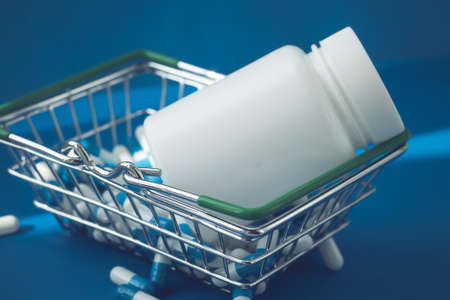 Pills in a grocery basket. Medicine capsules on the table. Buyer at the pharmacy. Ordering medicines online. Pills on a blue background in a box.の写真素材