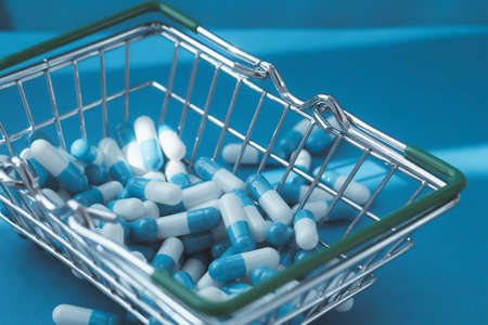 Pills in a grocery basket. Medicine capsules on the table. Buyer at the pharmacy. Ordering medicines online. Pills on a blue background in a box.の写真素材