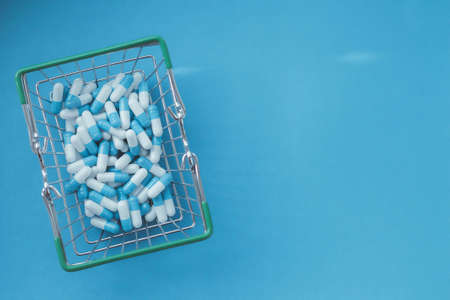 Pills in a grocery basket. Medicine capsules on the table. Buyer at the pharmacy. Ordering medicines online. Pills on a blue background in a box.の写真素材