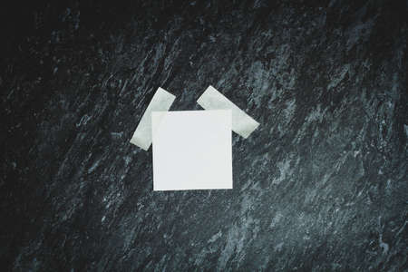 A white sheet of paper is glued with tape. Announcement template. Square sheet on a black background. Memorable note. Reminder on the wall.の写真素材