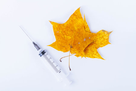 Autumn maple leaf and syringe with vaccine on white background. Vaccination against colds..の写真素材