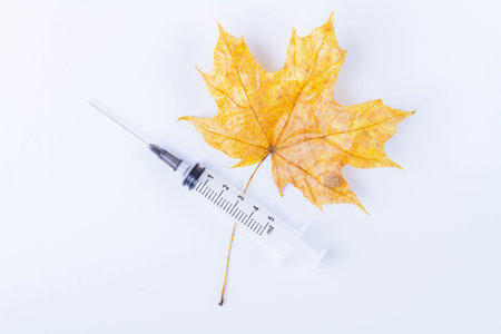 Autumn maple leaf and syringe with vaccine on white background. Vaccination against colds..の写真素材