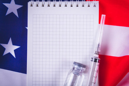 Syringe and vaccine on background of american flag. Vaccination in sasha. Blank notepad for vaccination records..の写真素材