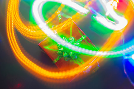 New Year's gift in a bright package against the background of Christmas decorations and bright lights of the garland..の写真素材