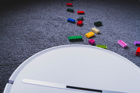 A robot vacuum cleaner cleans children's toys on the floor. Carpet and laminate cleaning. Assembling cubes with a robot vacuum cleaner..の写真素材