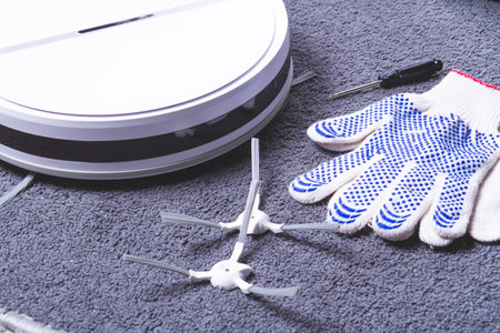 Maintenance of the robot vacuum cleaner. Replacement of brushes and filter. The master repairs the vacuum cleaner. Gloves and a master's tool.の写真素材