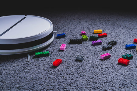 A robot vacuum cleaner cleans childrens toys on the floor. Carpet and laminate cleaning. Assembling...