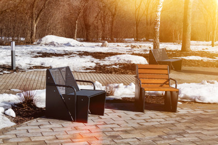 Wooden bench in the spring park. Bright spring sun and snow in the park. Place to rest for a walk. Morning walk.の写真素材