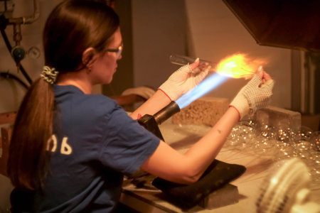 A young girl blows glass toys. Glass blower at a factory. Fire and glass.