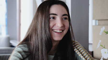 A young smiling girl is sitting in a cafe. A young woman in a cafe communicates with her friend. Positive emotions, laughter. Girl with a blanket in a cafeの写真素材