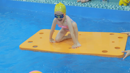 Little girl in the pool for a fee. Child, girl learns to swim in the pool. A cute little girl is studying in the pool. Child in the pool on a foam raftの写真素材