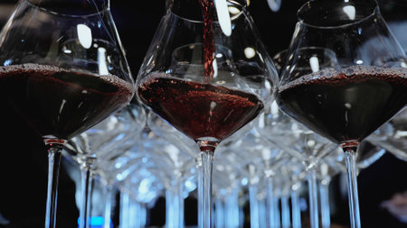 Glasses of wine on the bar. Red wine in glasses. Close-up shot of pouring wine into glassesの写真素材