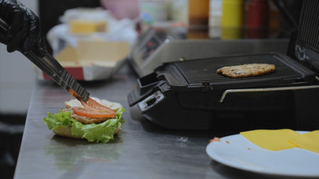 Cooking hamburger in the kitchen. Cooking a delicious burger. The chef puts onion rings while preparing a hamburger. Cooking hamburgers on a hot grill pan.の写真素材