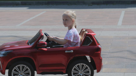 A little girl rides a car. The girl is driving a childrens car.
